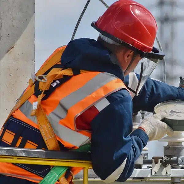 électricien au travail en extérieur sur un chantier avec un casque et un gilet fluo orange