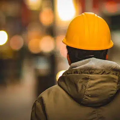Fabrice Heuveline, de l'entreprise Heuvelec, de dos avec un casque de chaniter jaune et une parka kakai. Le fond est flou.
