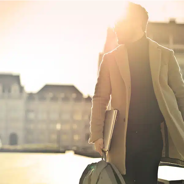 un homme qui marche dans la rue vêtu d'un manteau élégant avec un sac à la main, à contre-jour