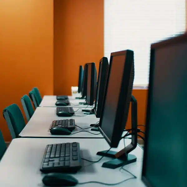 salle informatique dont l'installation a été réalisée par Heuvelec. 5 postes de travail avec ordinateur, clavier, souris alignés sur une grande table avec des chaises vertes.