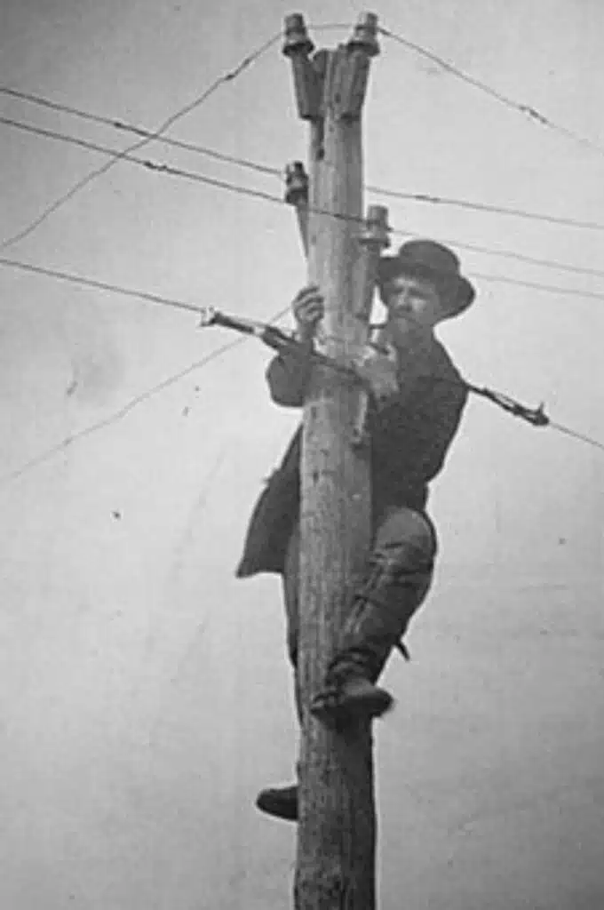photographie ancienne d'un électricien grimpé sur un poteau électrique, en noir et blanc.