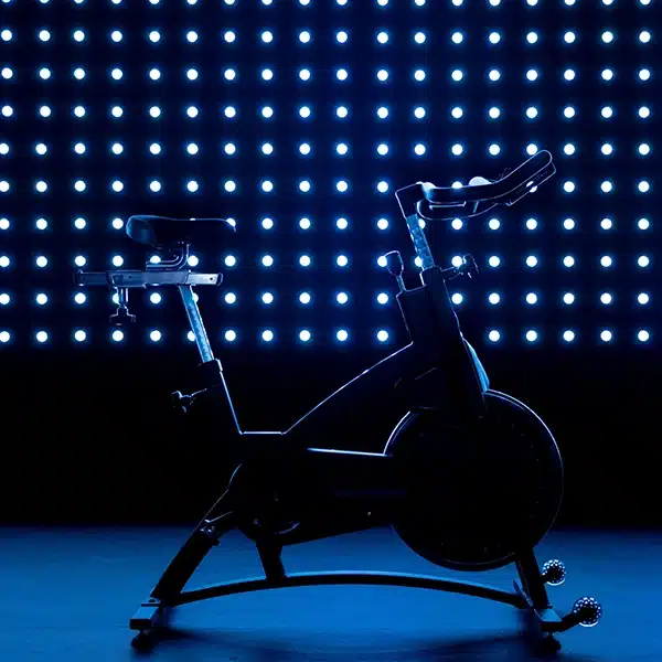 vélo d'appartement dans une salle de fitness, dans la pénombre devant un mur couvert de led allumées